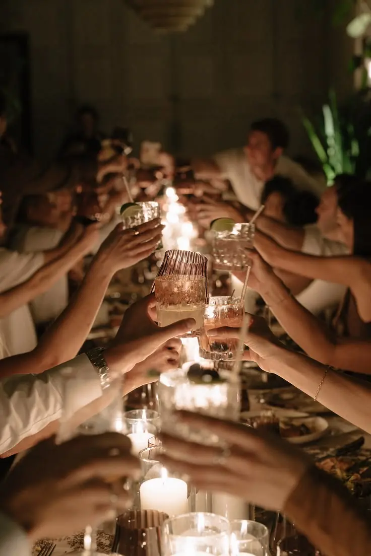 A group raising glasses together over a candlelit dinner table
